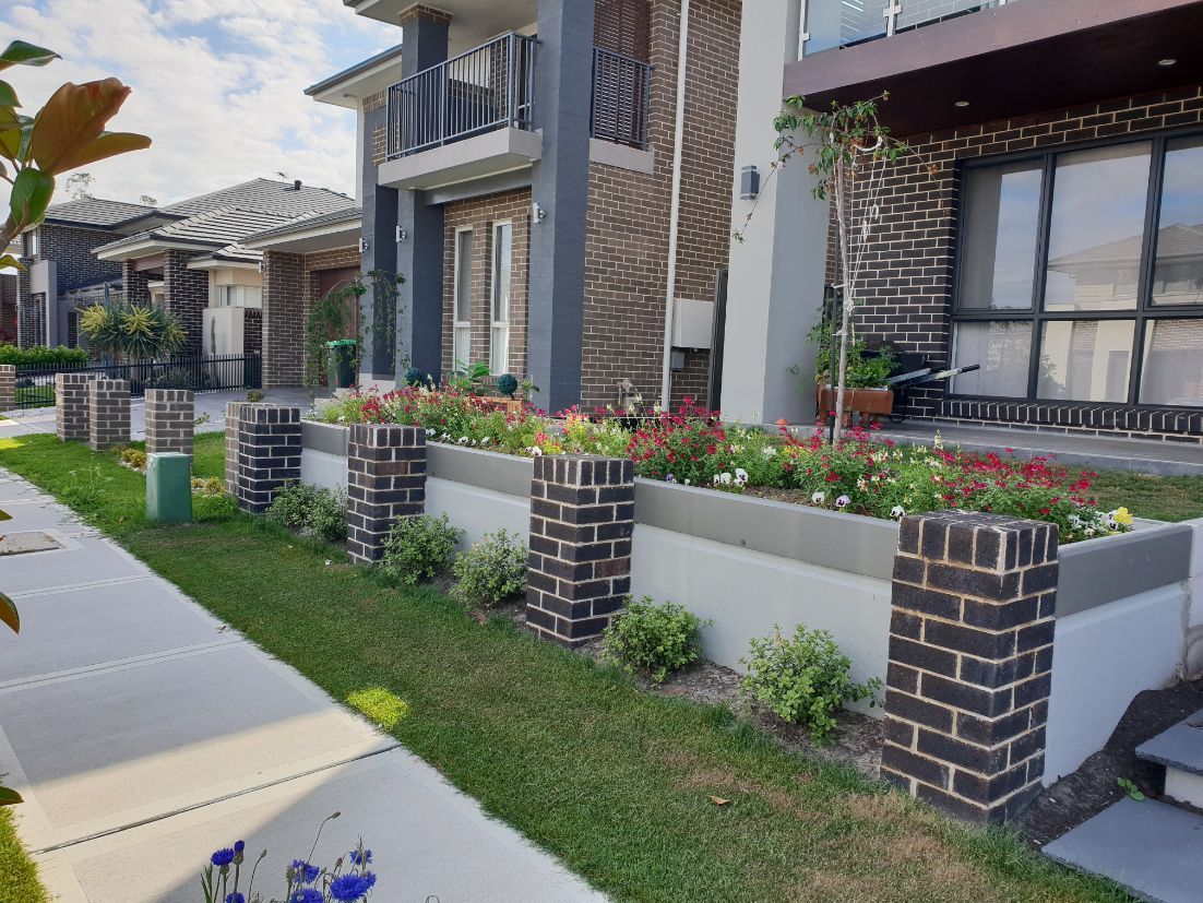 a row of brick planters filled with flowers in front of a house .