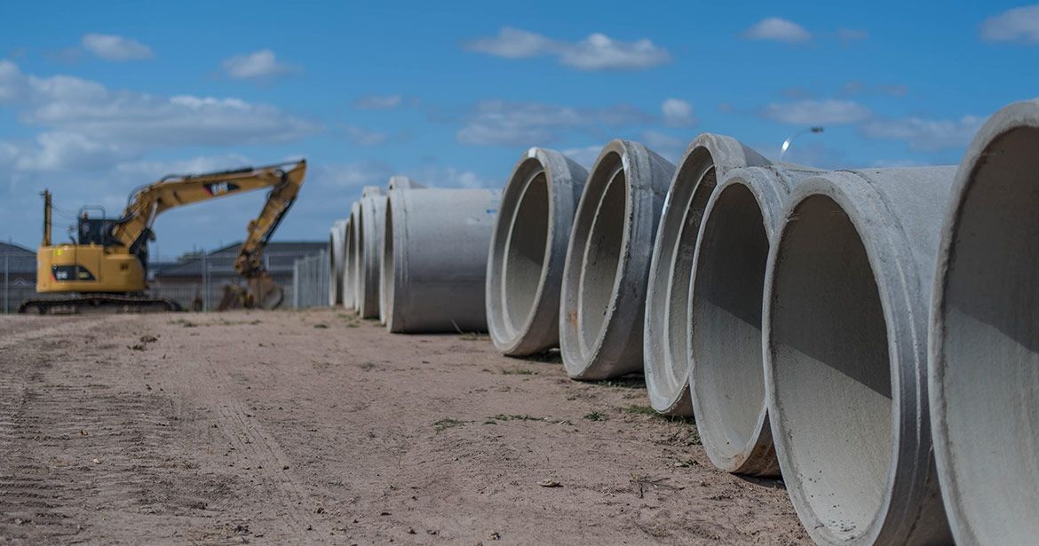 a row of concrete pipes sitting on top of a dirt field with a bulldozer in the background .