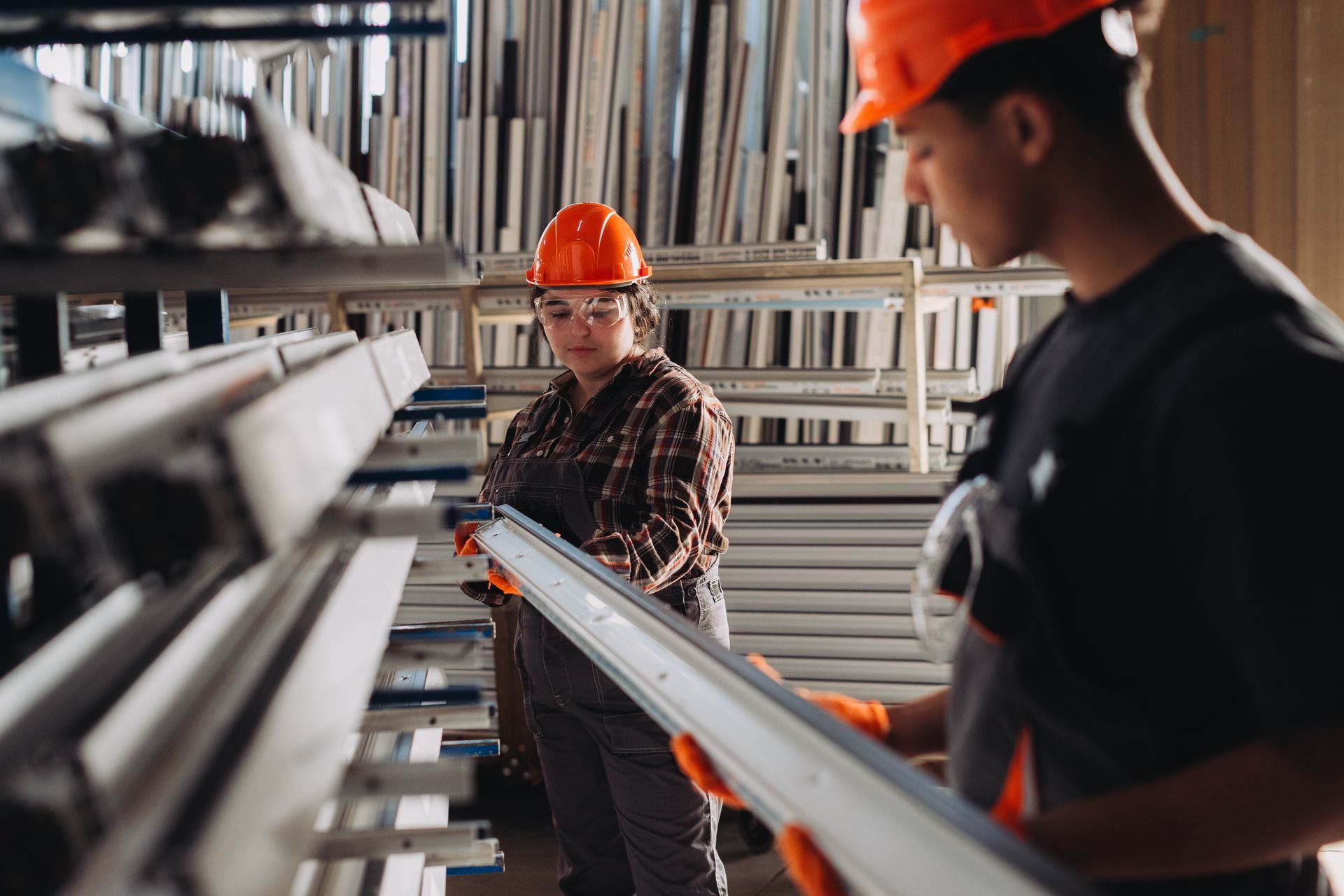 Two workers holding manufactured aluminium window profiles in supply area.