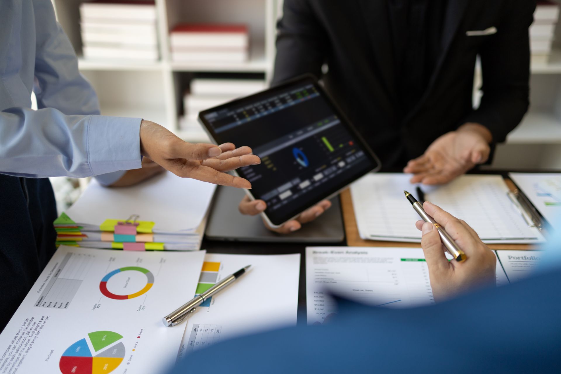 A group of people are sitting at a table looking at a tablet.