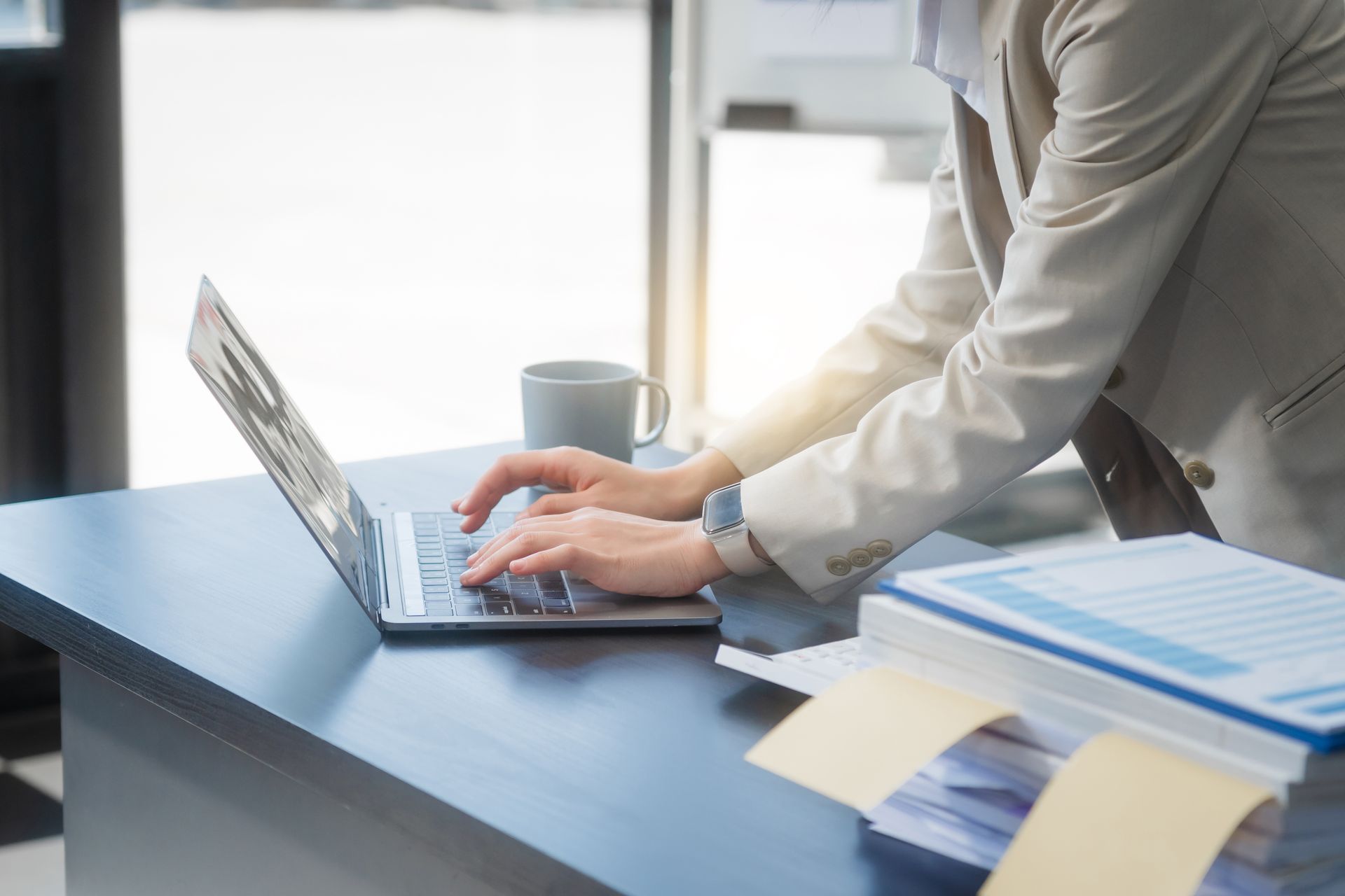 A woman is typing on a laptop computer at a desk.