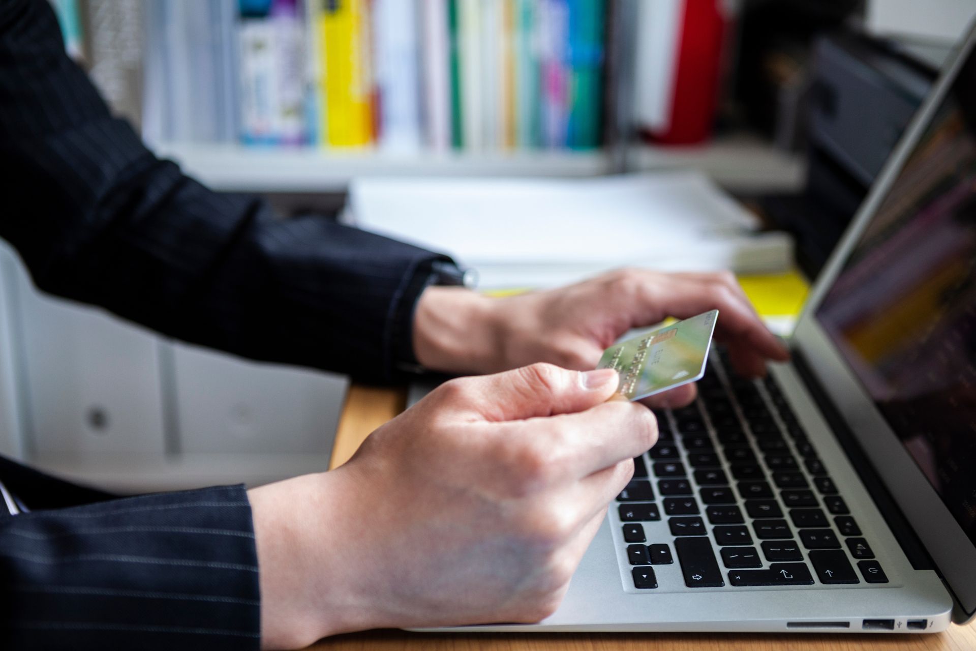 A person is holding a credit card in front of a laptop computer.