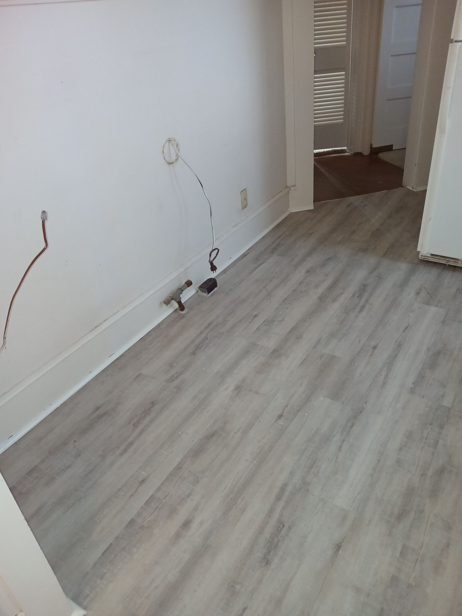 Interior room with unfinished walls, exposed wires, and light wood-look flooring. Doorway visible in background.