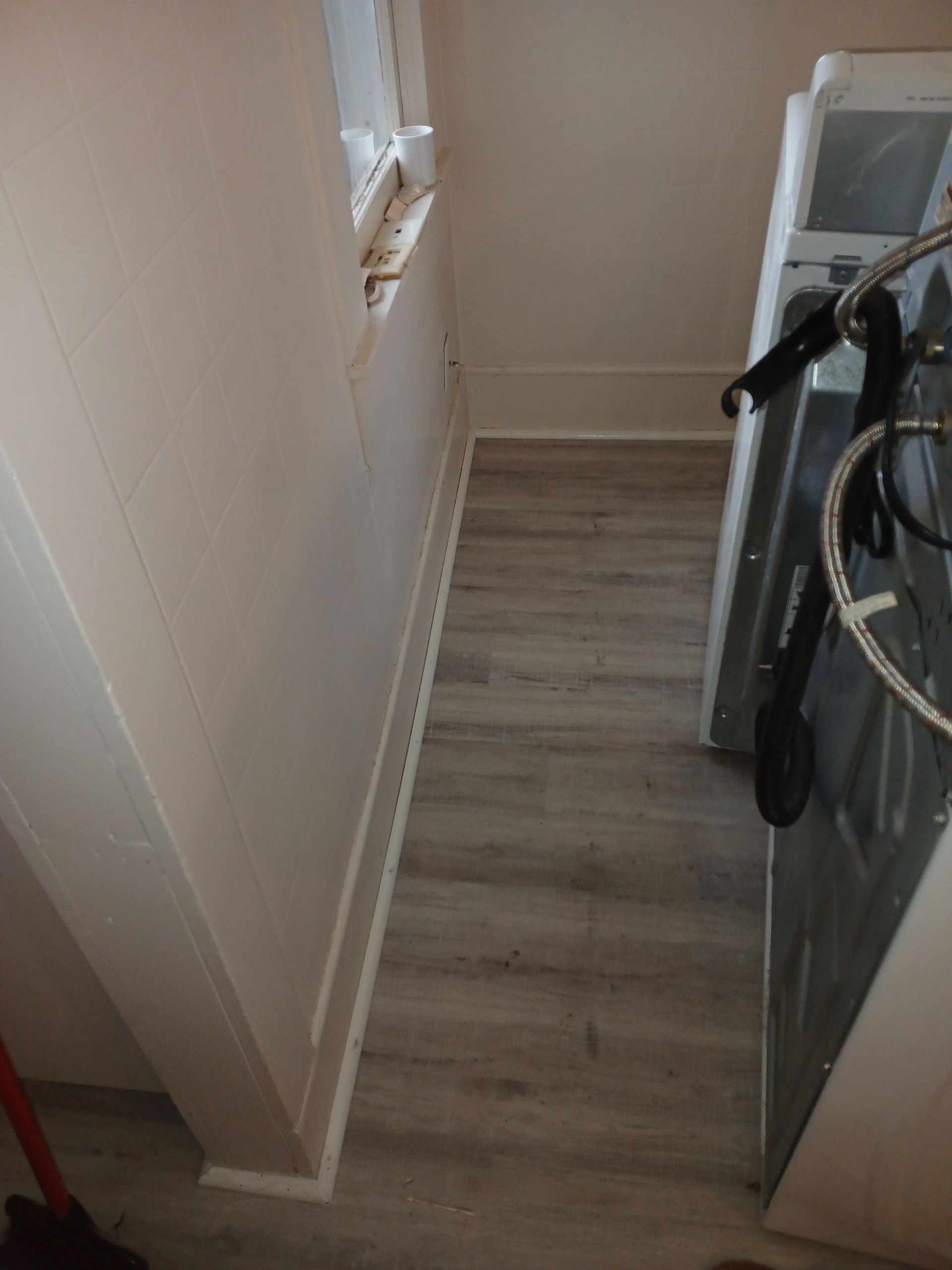 Narrow room with gray flooring, baseboard trim, and a partially visible appliance.