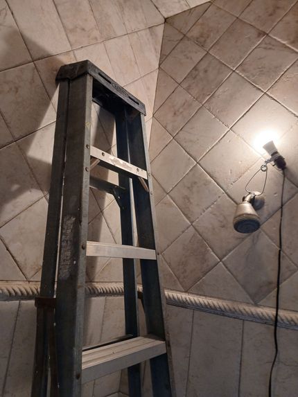 Ladder leaning against tiled wall, lit by a small spotlight, inside a room.