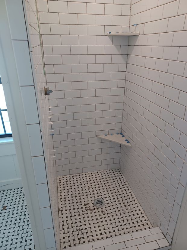 White tiled shower with built-in shelves and a drain. A small, built-in seat is present.