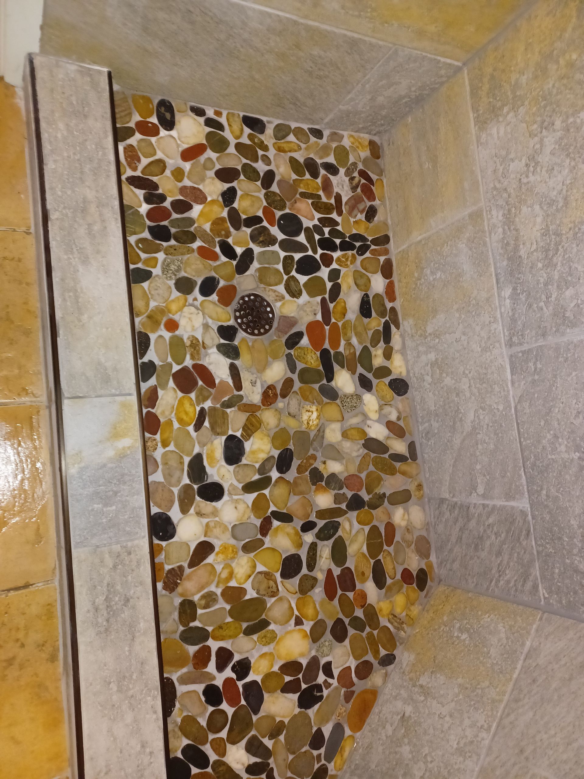 Shower niche with pebble tile, featuring a drain. Beige and brown tones.