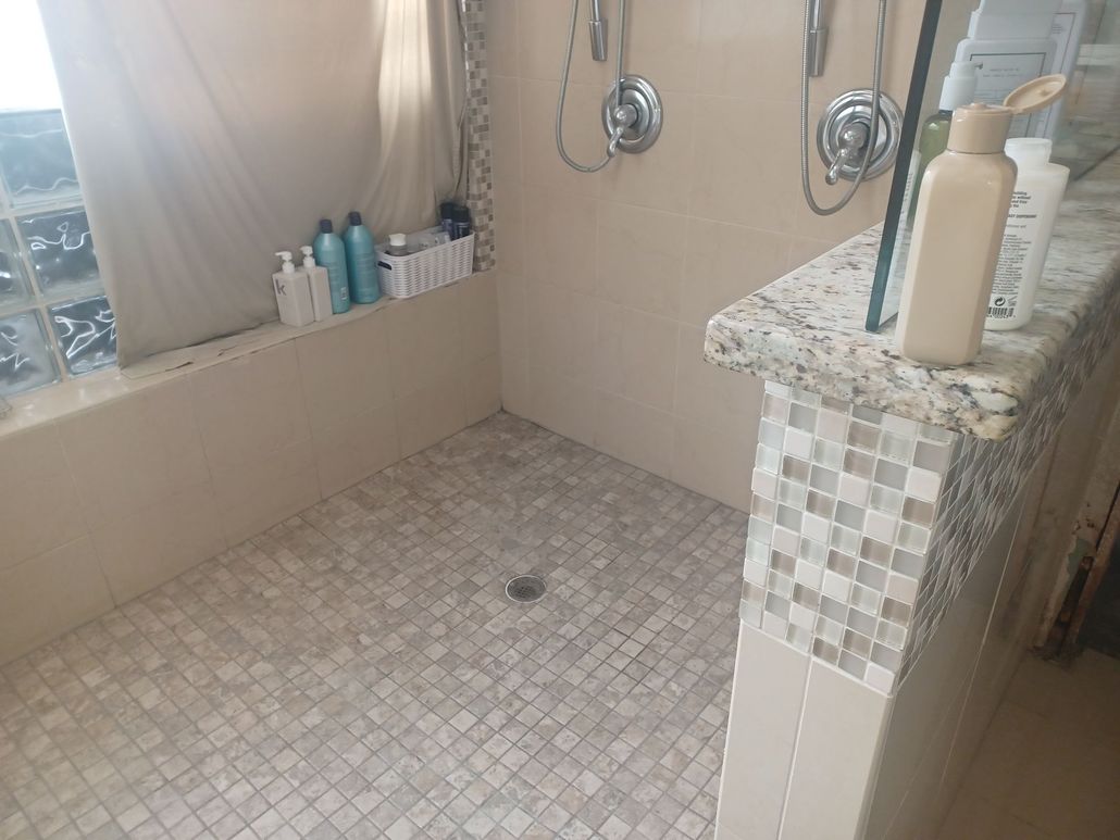 Shower with tiled floor, multiple showerheads, and a low wall with a stone top.
