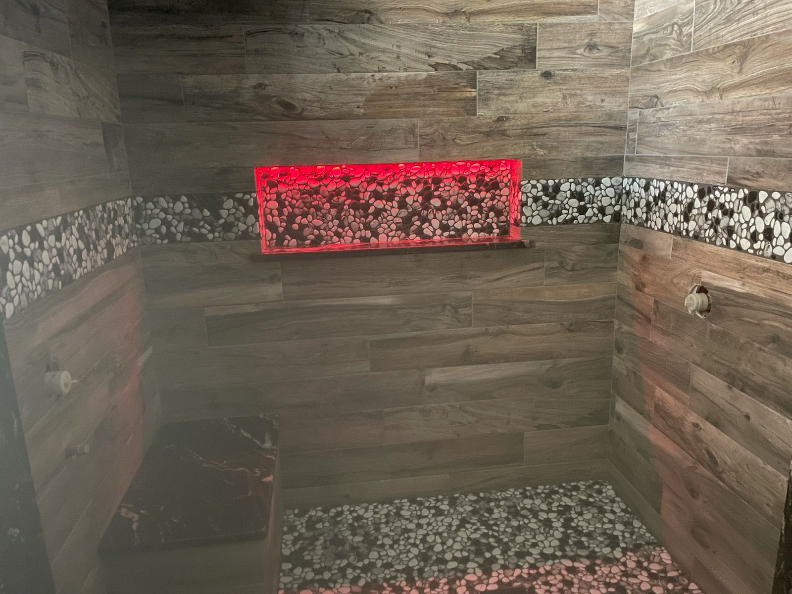 Red light sauna interior with wooden tile walls, stone floor, and glass enclosure.
