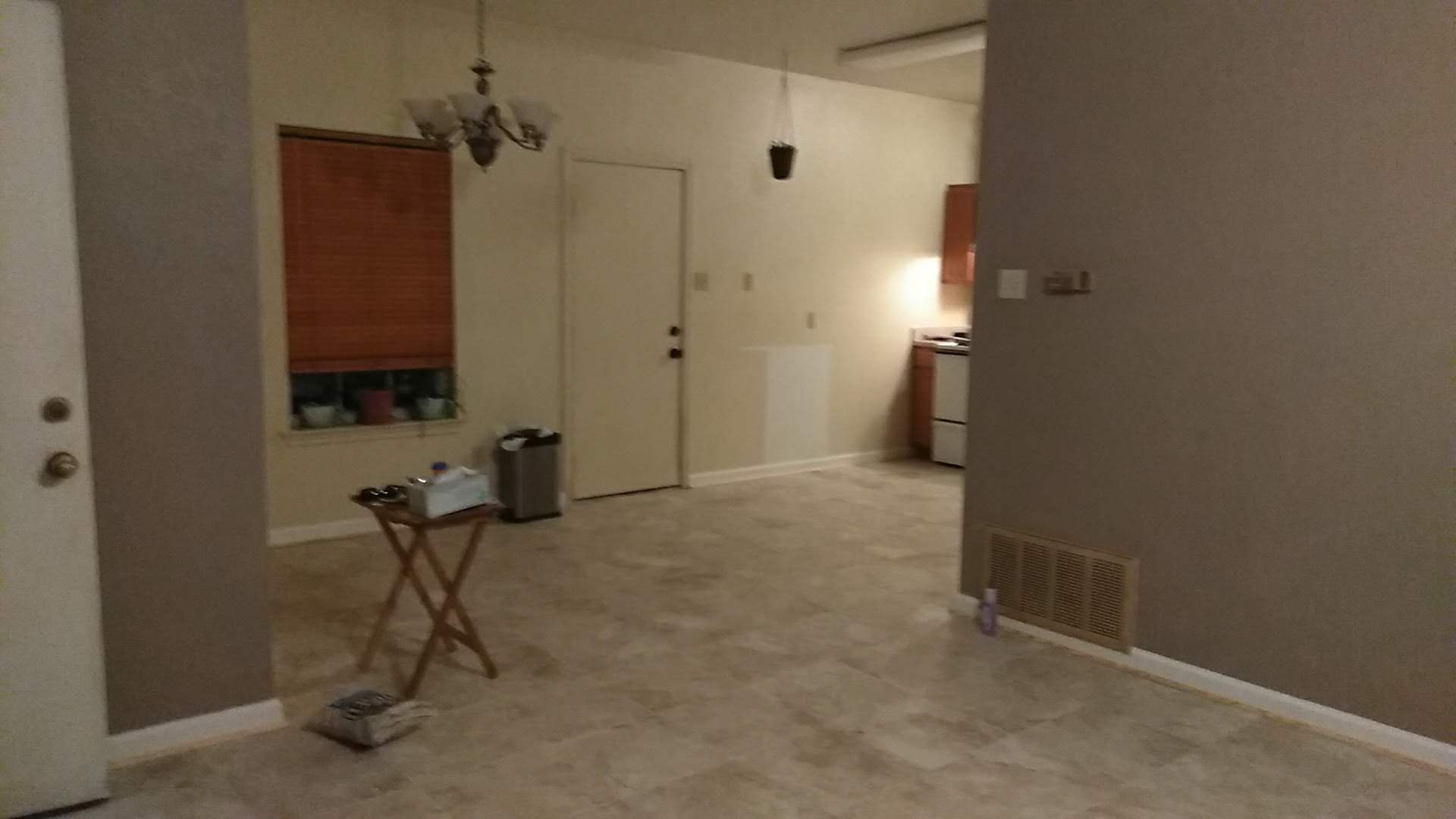 Interior view of a living space with beige carpet, gray walls, and a view into a kitchen area.