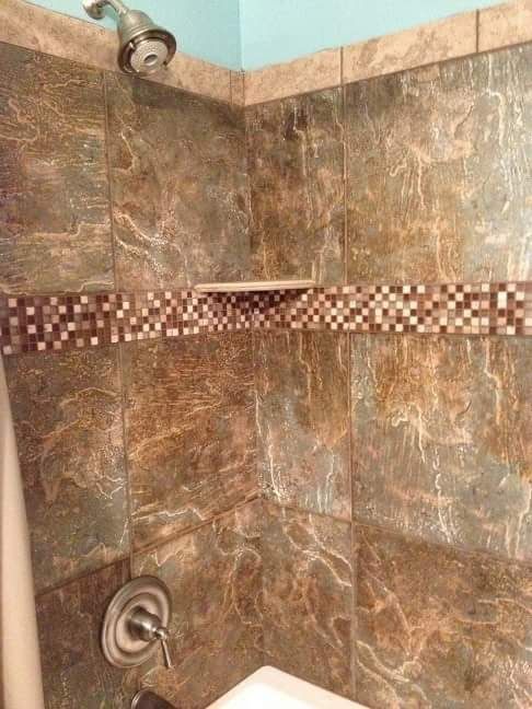 Shower with brown marble-look tiles, a decorative mosaic tile band, and a built-in shelf. A silver showerhead is visible.