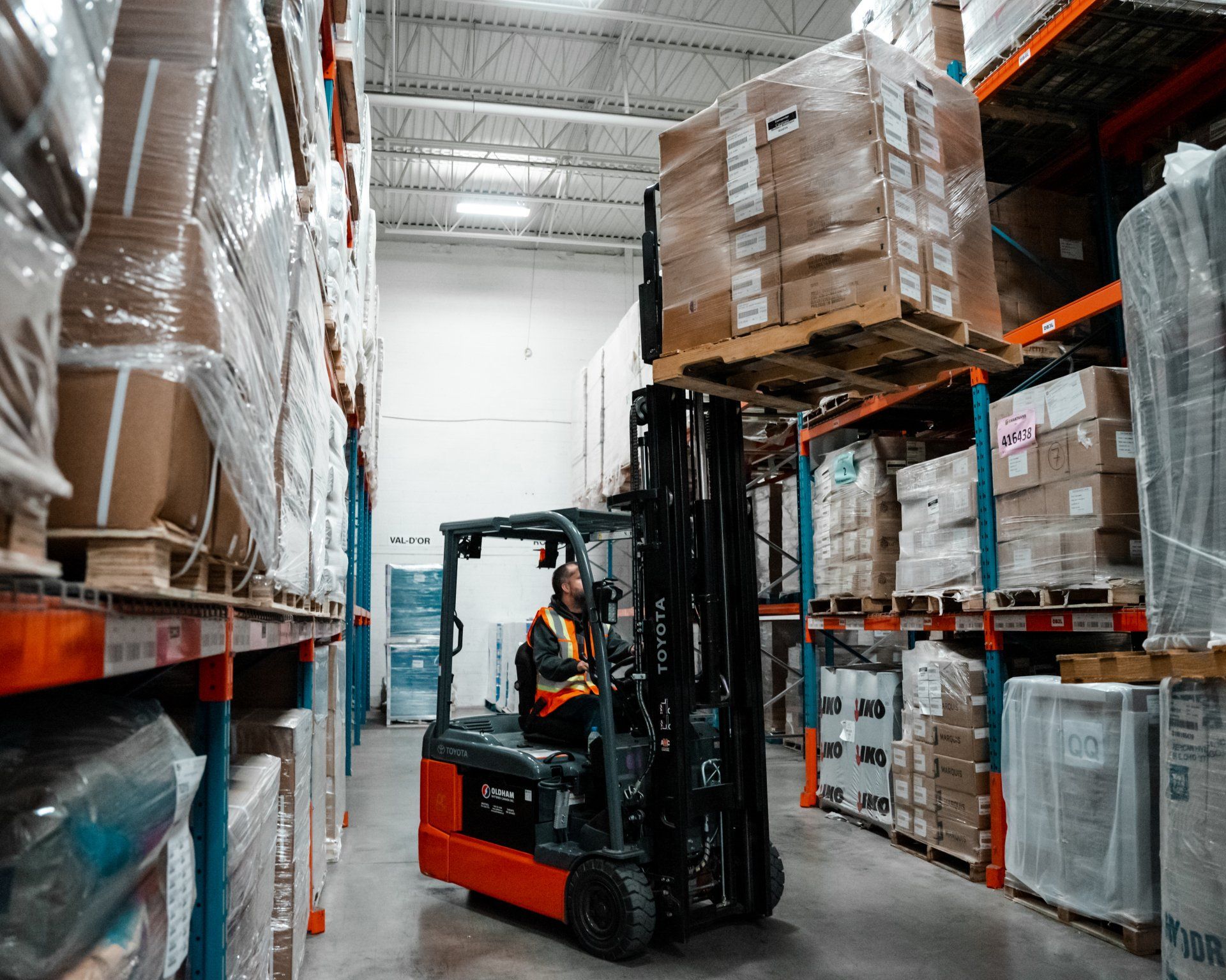 Un homme conduit un chariot élévateur dans un entrepôt transportant une palette de boîtes.