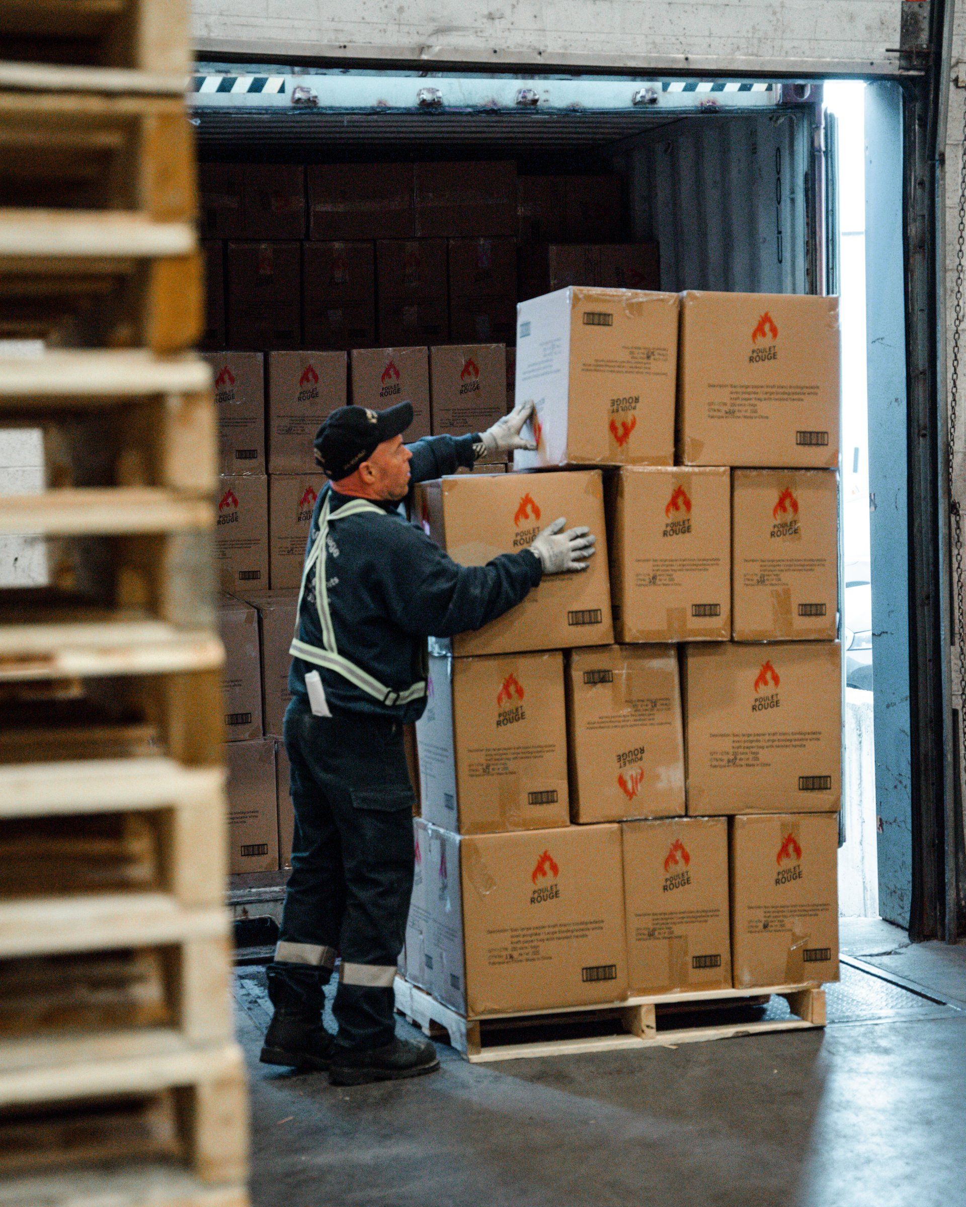 Un homme empile des boîtes sur une palette dans un entrepôt.