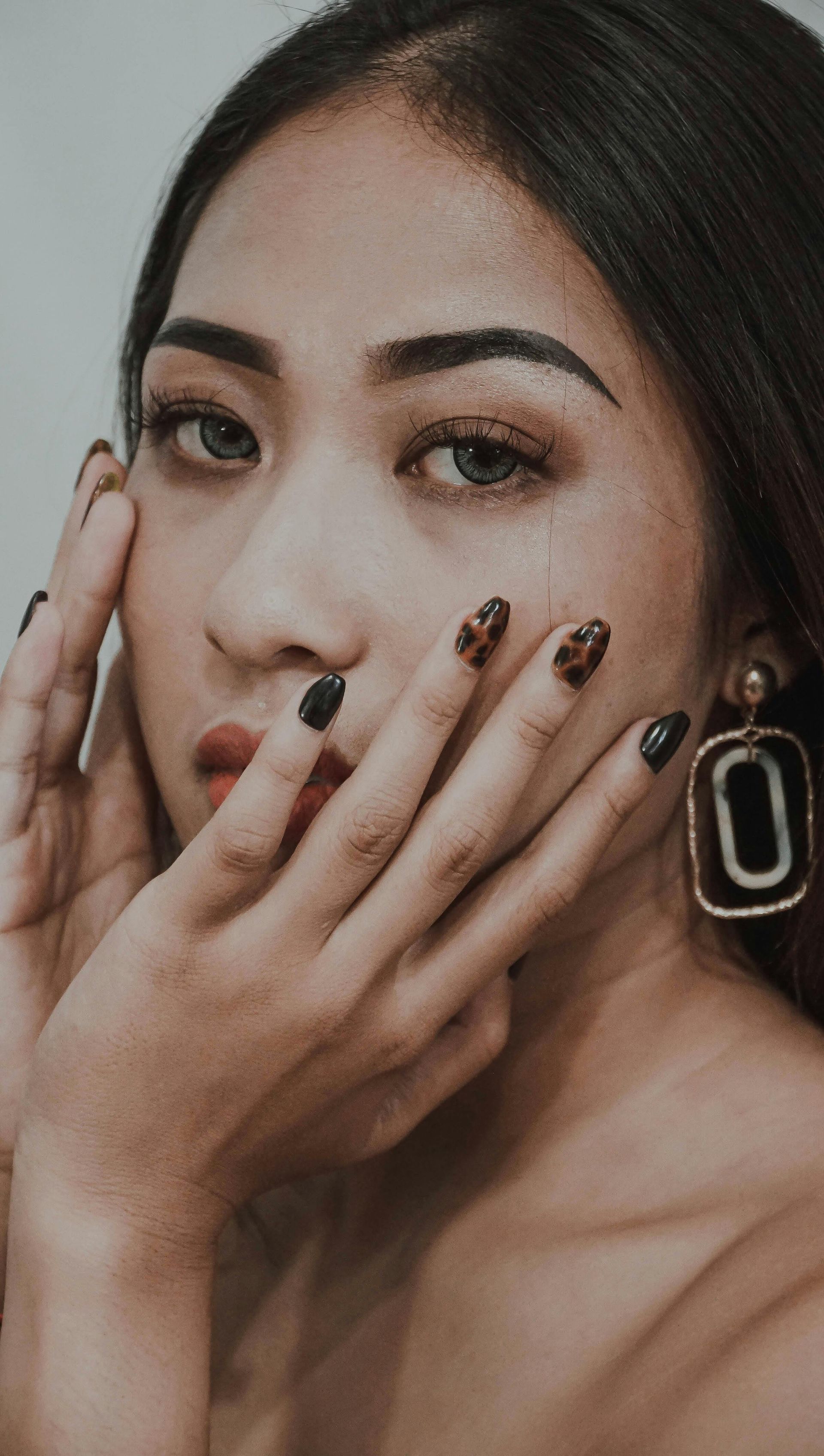 A close up of a woman covering her face with her hands and wearing earrings.