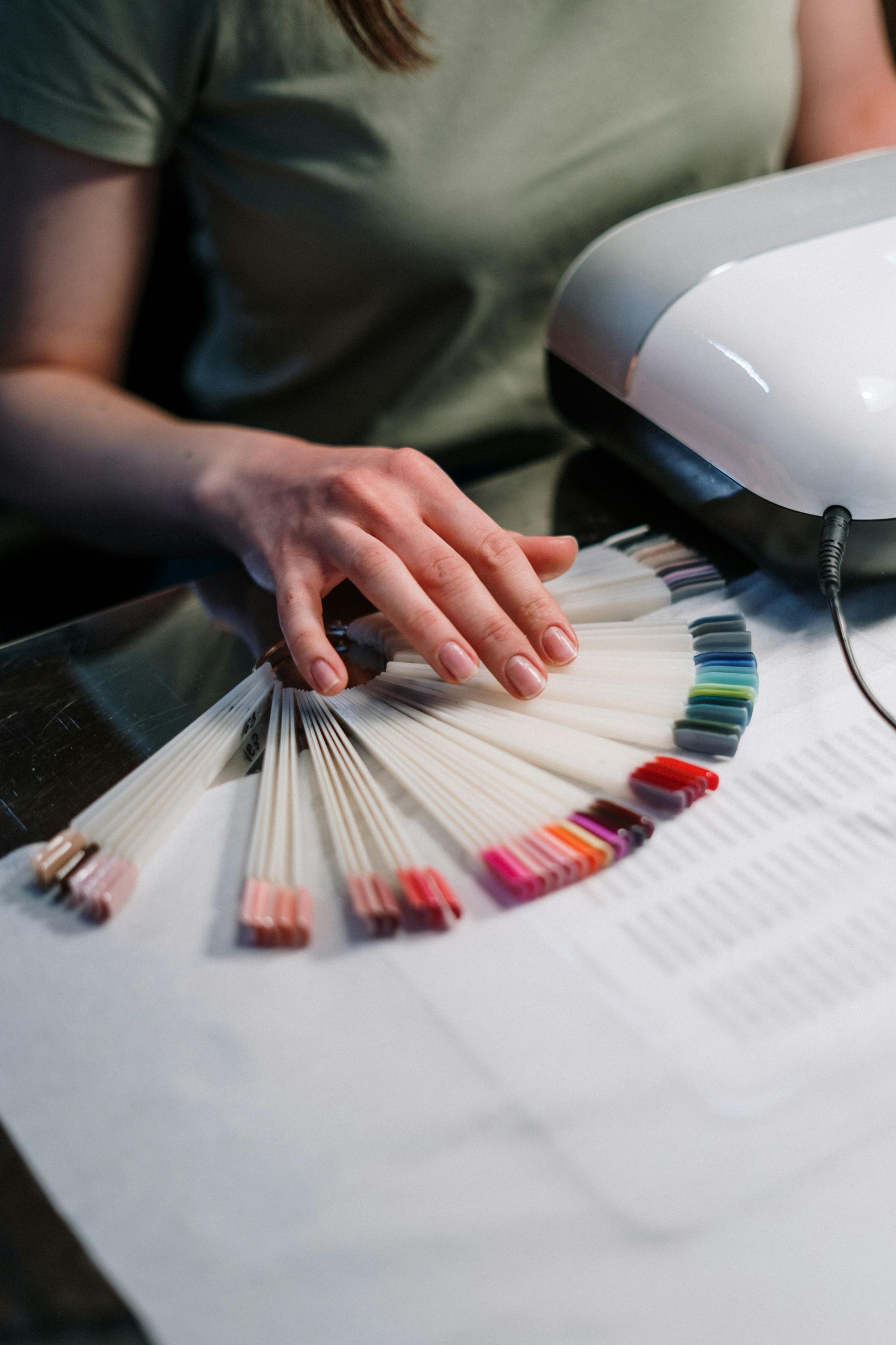 A woman is sitting at a table holding a fan of nail polish samples.