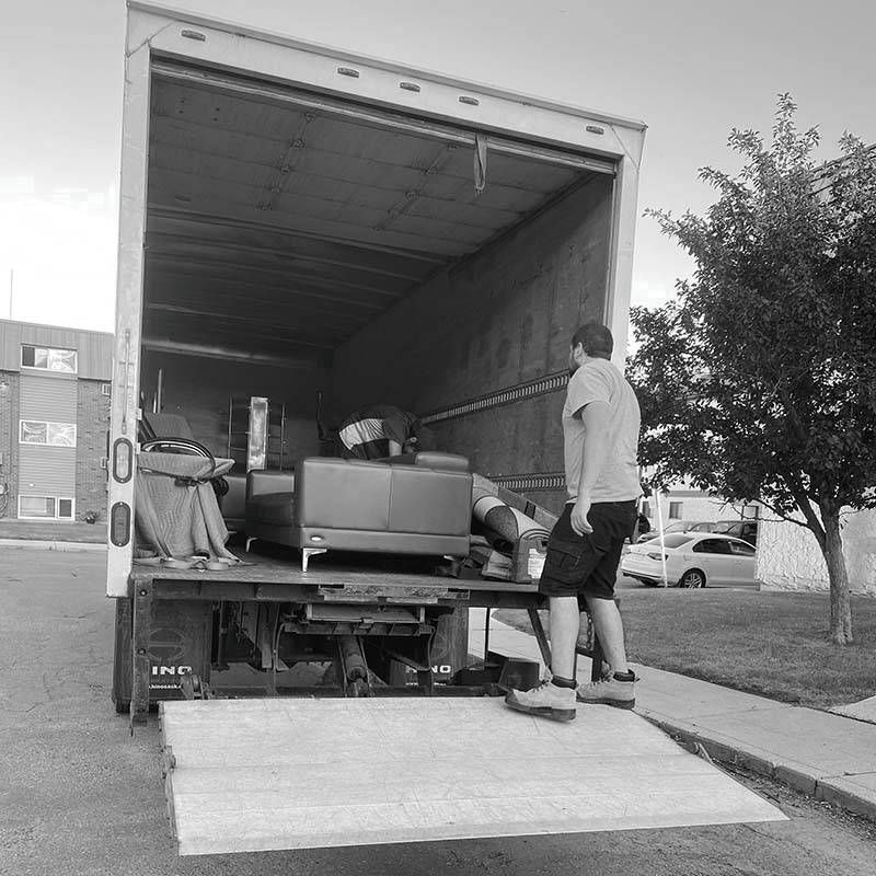 A man is standing on the ramp of a moving truck.