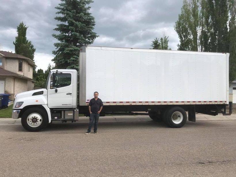 A man is standing in front of a large white truck