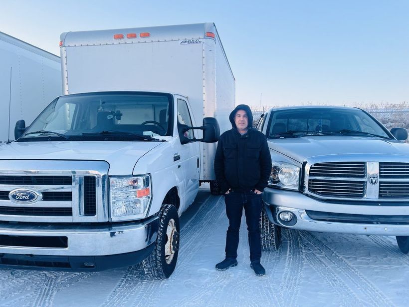 A man is standing in front of two trucks in the snow.