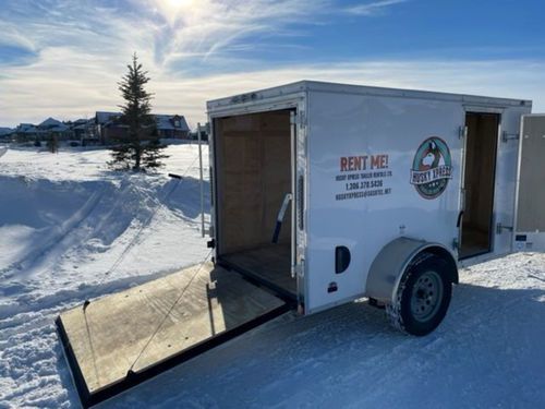 A white trailer is parked in the snow with the door open.