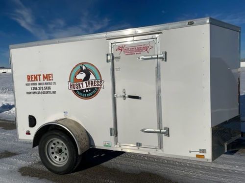 A white trailer with a horse on it is parked in the snow.