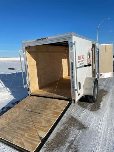 A white trailer with the door open is parked on a snowy road.