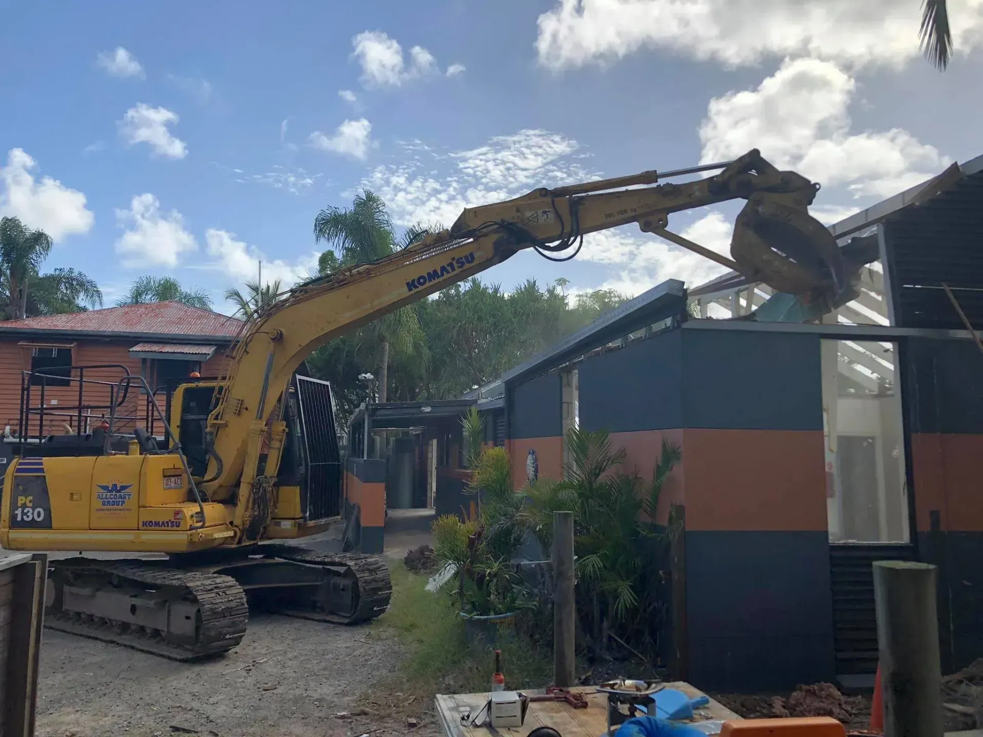 Yellow Komatsu excavator demolishing a building, tearing into the roof structure.