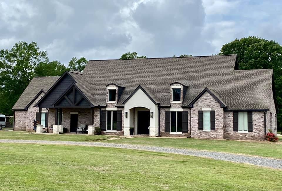 Large brick house with dark shutters, gabled roof, and gravel driveway.