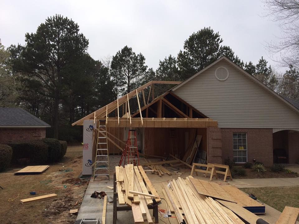 Construction of a garage addition on a beige brick house, with wood framing and materials visible.