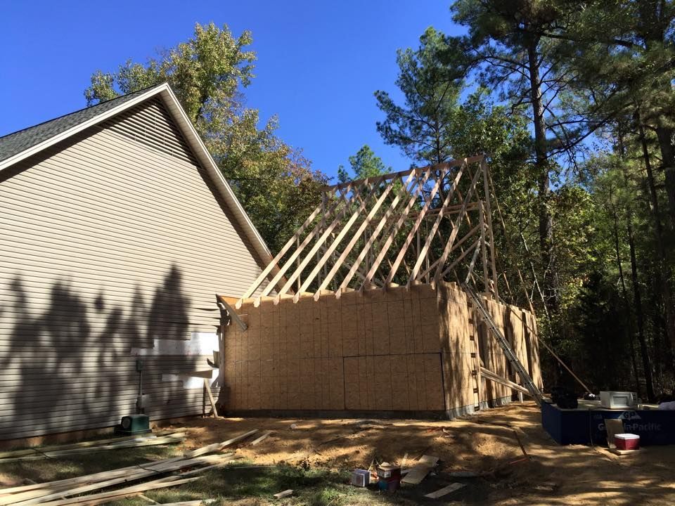 Construction of a shed or garage next to a house; unfinished walls, rafters, and trees.