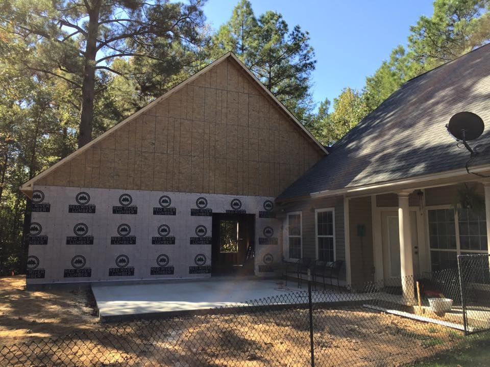 Construction site: New addition to house with plywood, siding, and concrete patio.
