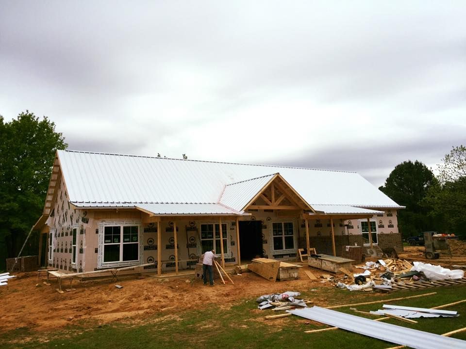 Construction of a house with a white metal roof, wood framing, and a man working outside on a cloudy day.