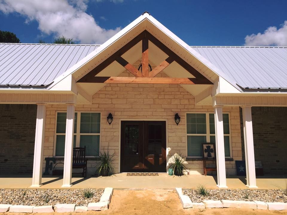 Exterior of a house with a stone facade, covered porch, and metal roof on a sunny day.