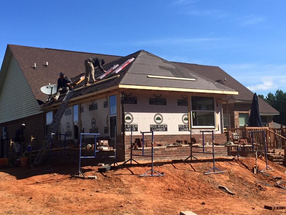 Construction workers roofing an addition to a brick house on a sunny day.
