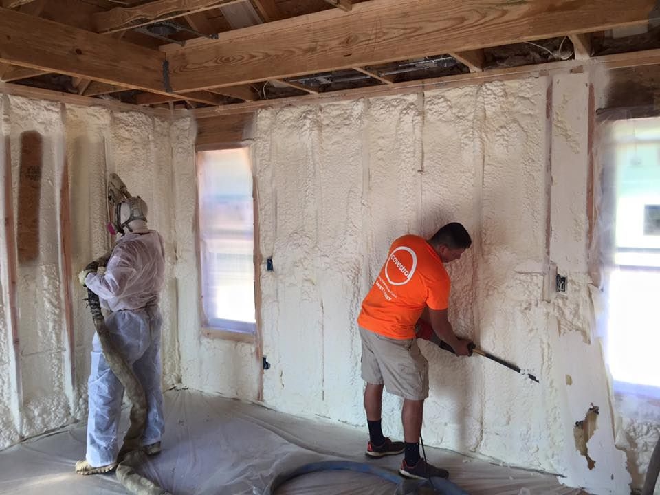 Two workers spraying insulation foam inside a building. One wears protective gear.
