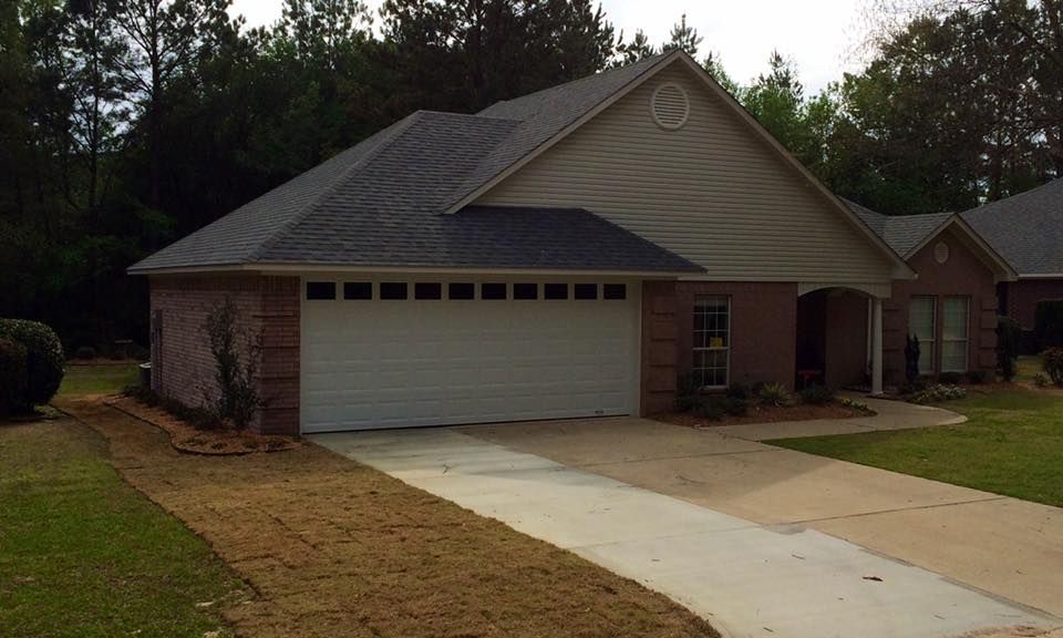 A brick house with a gray roof and attached garage, with a driveway and front yard.
