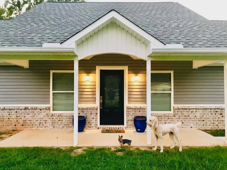 House with gray siding and brick base, porch with dogs in front.