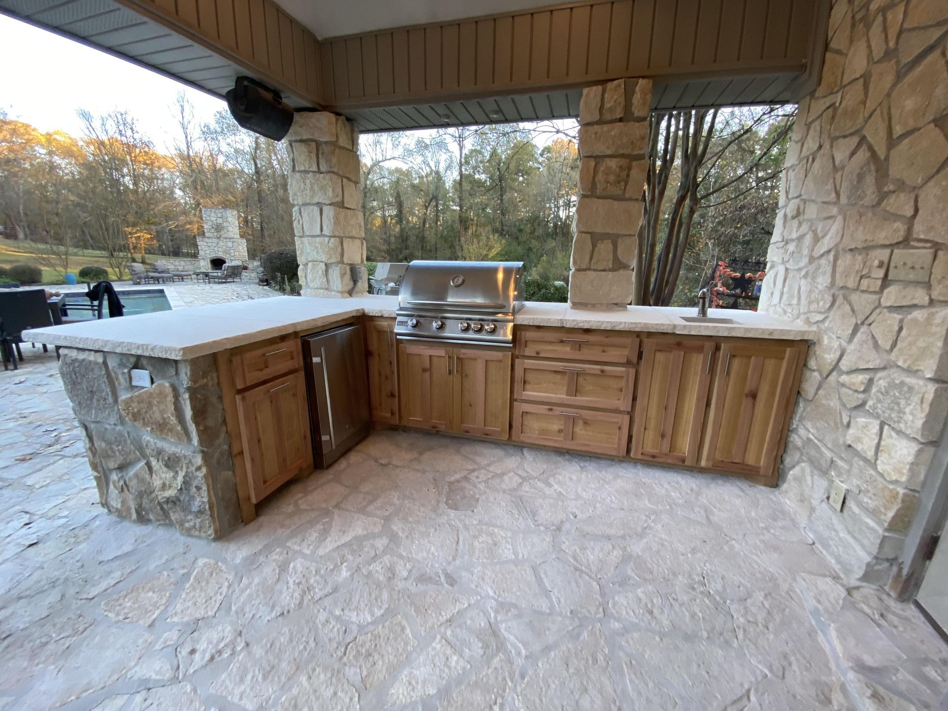 Outdoor kitchen with stone and wood cabinetry, grill, sink, and countertop.  Located on a stone patio.