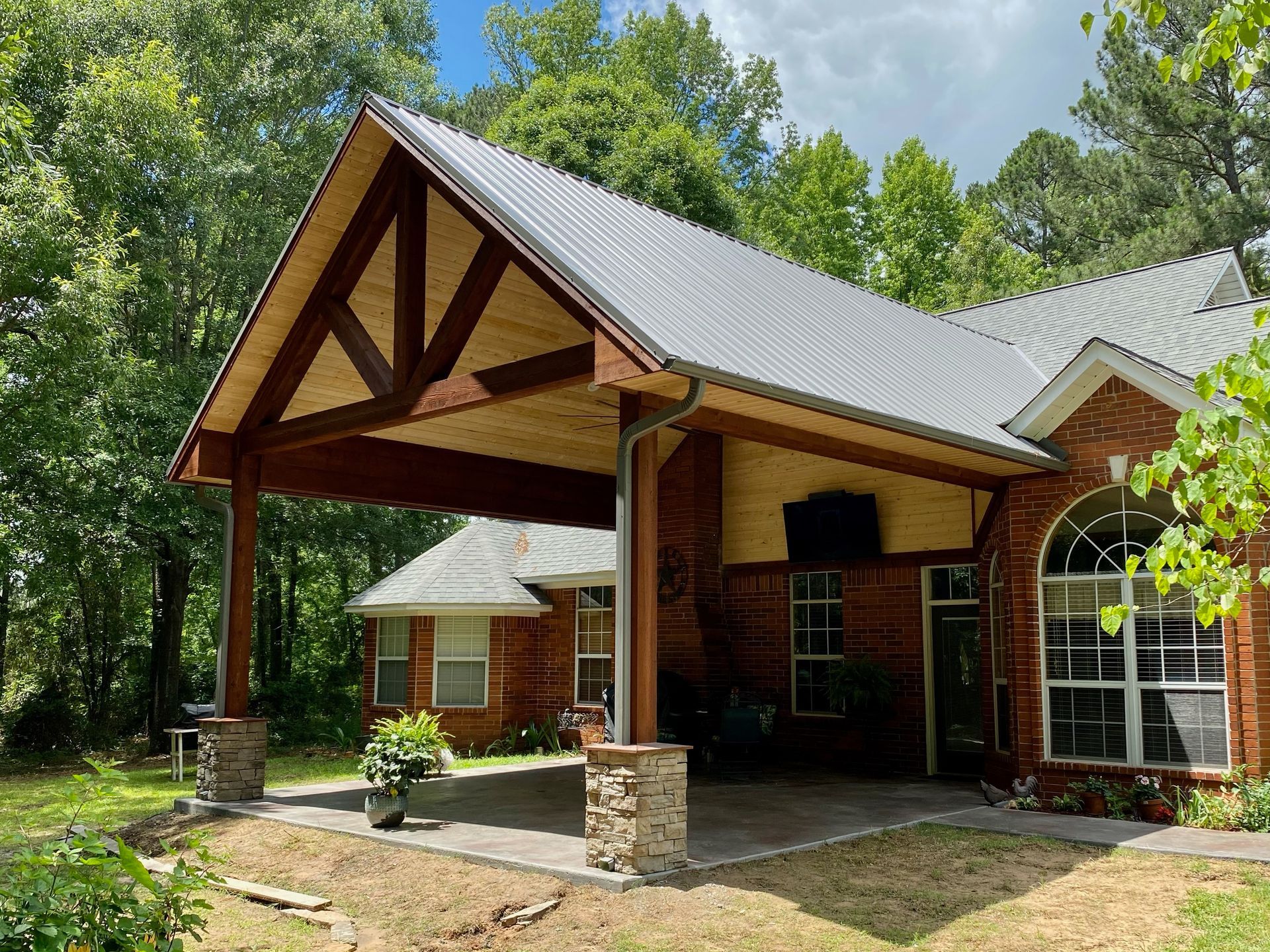 Brick house with a covered patio, featuring a wooden frame and metal roof.