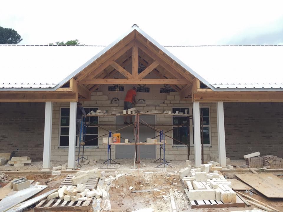Construction workers building a stone facade on a building with a gabled roof and wooden beams.