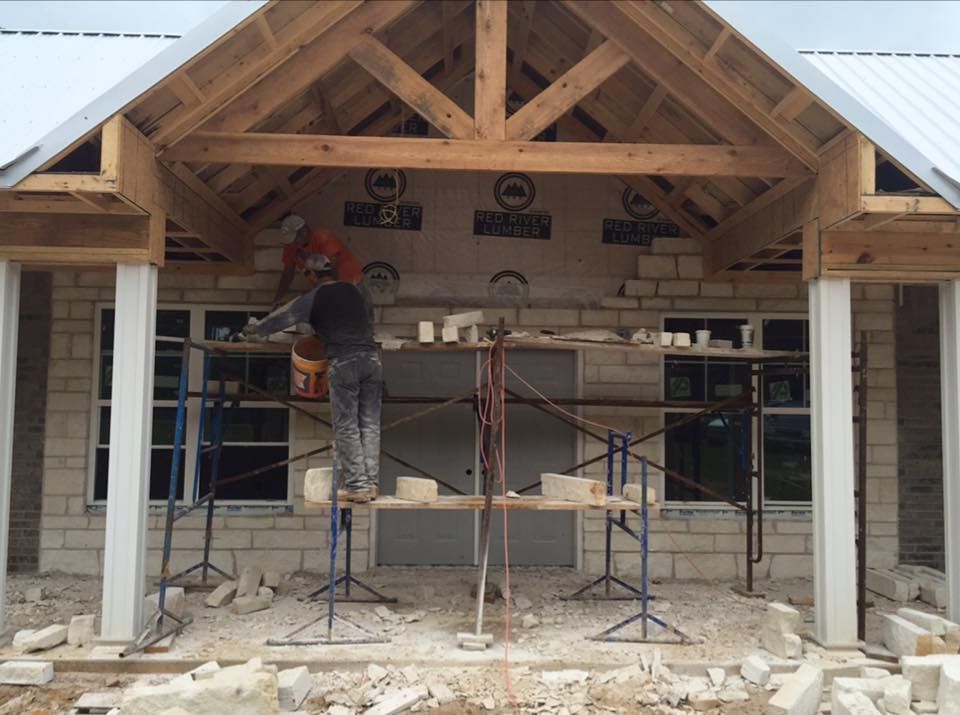 Construction workers laying brick on a building under a wooden roof.