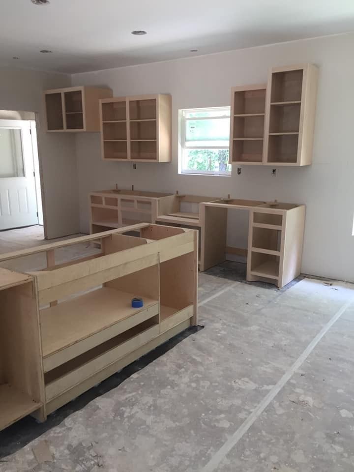 Unfinished kitchen with light wood cabinets installed on walls, bare counters, and concrete floor.