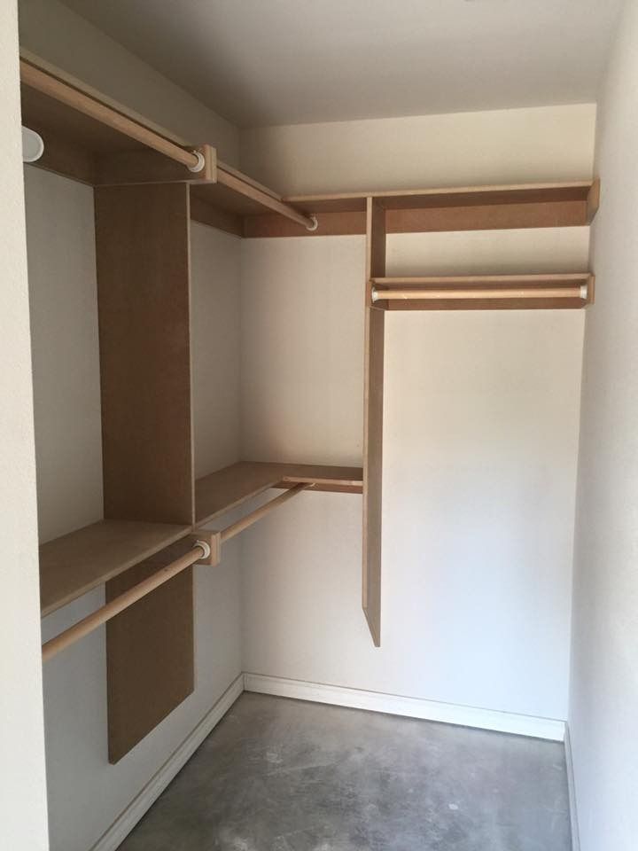 Empty closet with unfinished wooden shelves and clothing rods; white walls and floor.