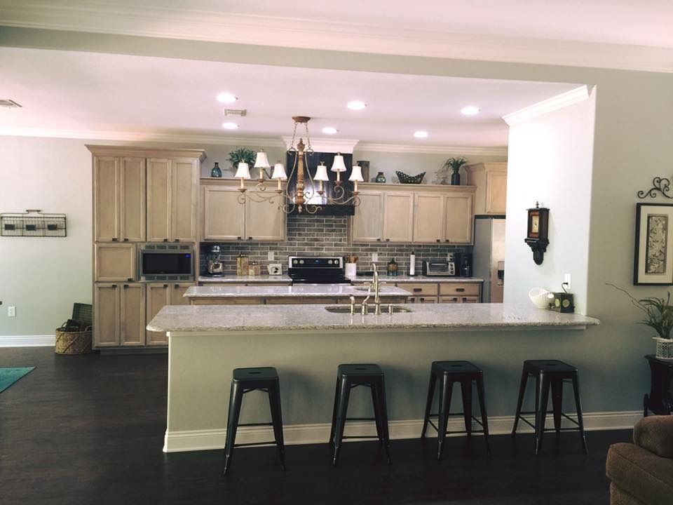 Kitchen with light wood cabinets, granite countertop, breakfast bar with black stools, and chandelier.
