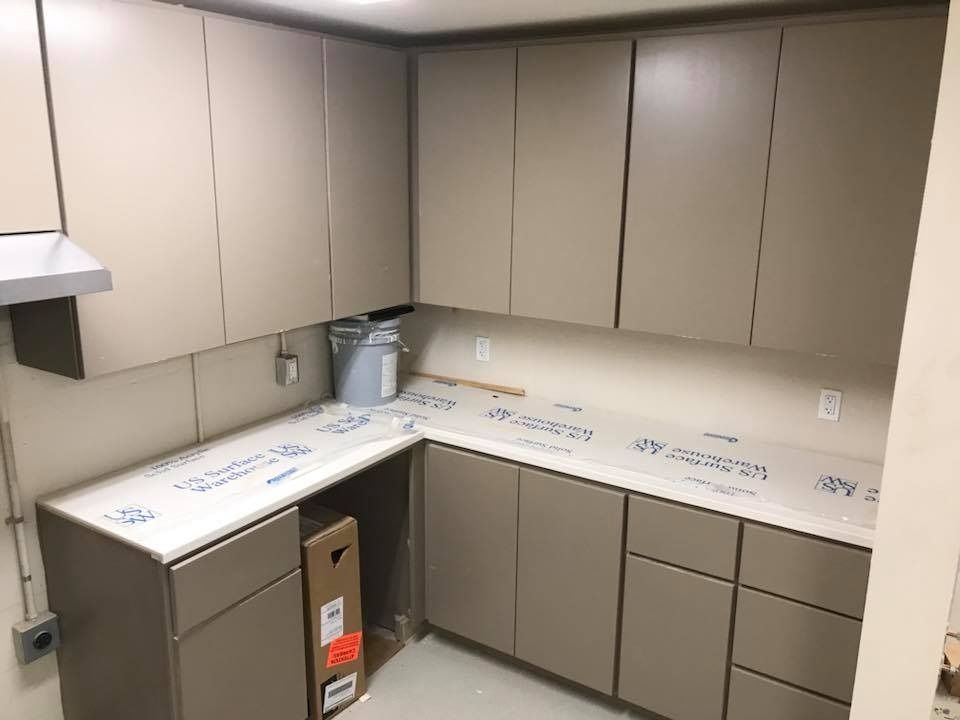 Kitchen with neutral-toned cabinets, countertop covered in protective film, unfinished walls, and a small range hood.
