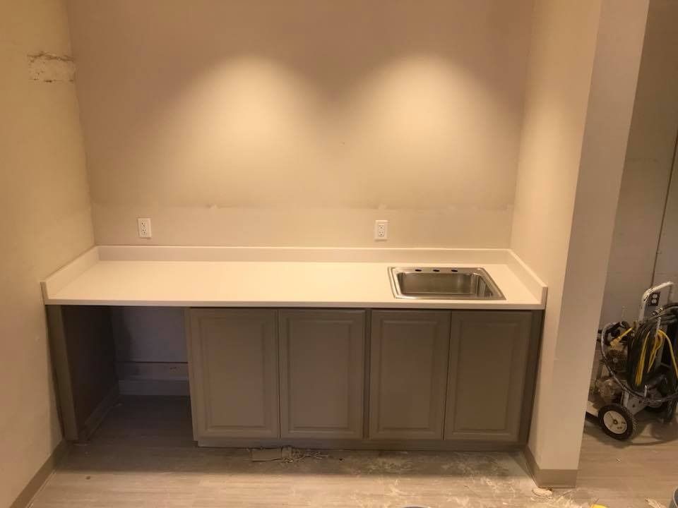 A small kitchen area with a countertop, cabinets, and a sink. Beige walls and a light countertop.