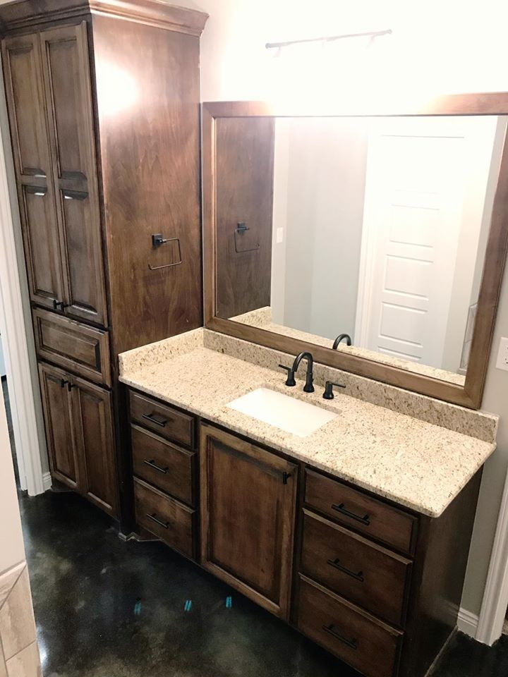 Bathroom vanity with brown cabinetry, granite countertop, mirror, and tall storage cabinet.