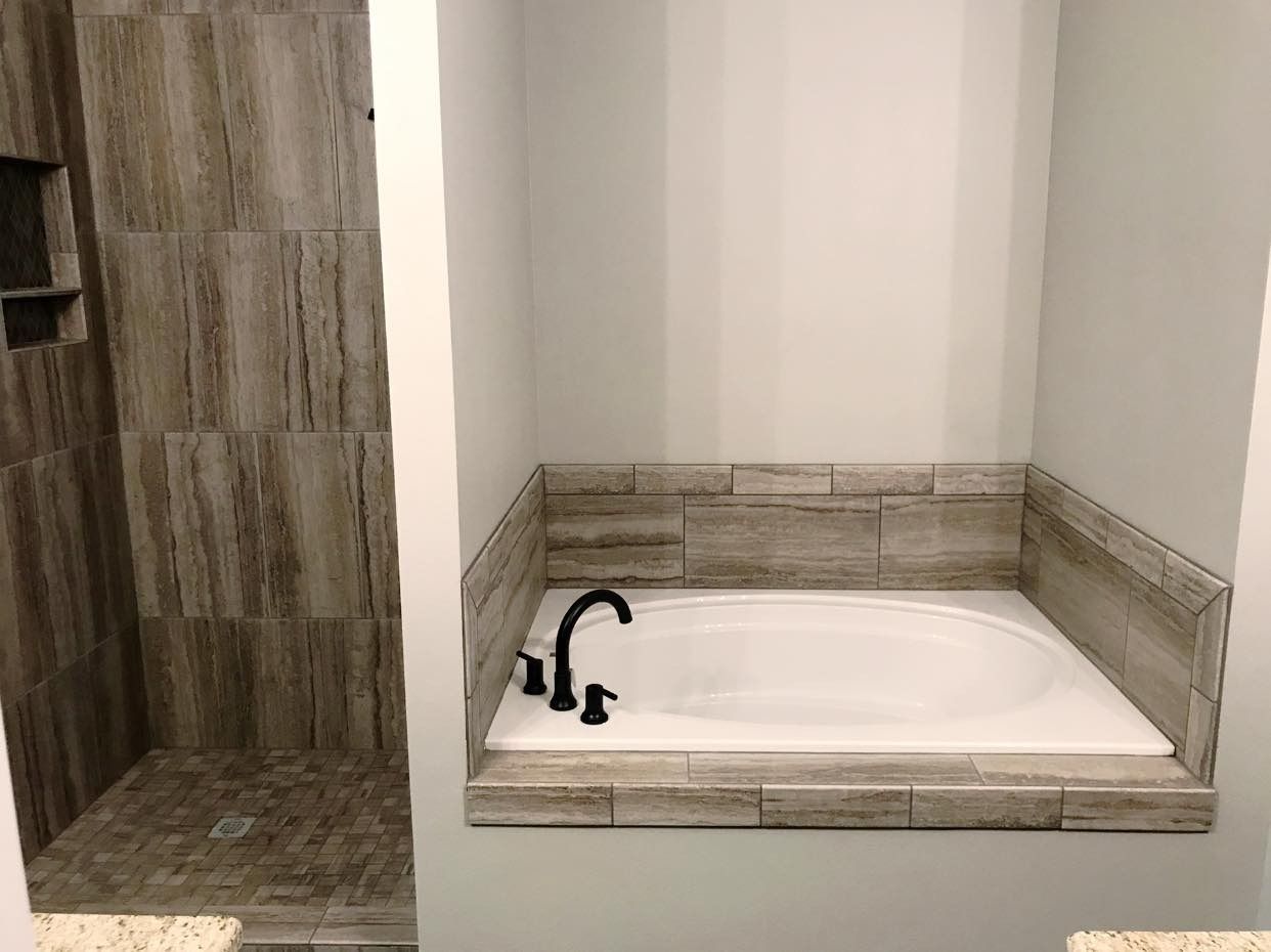 Bathroom with a built-in white bathtub surrounded by light brown tile, next to a tiled shower.