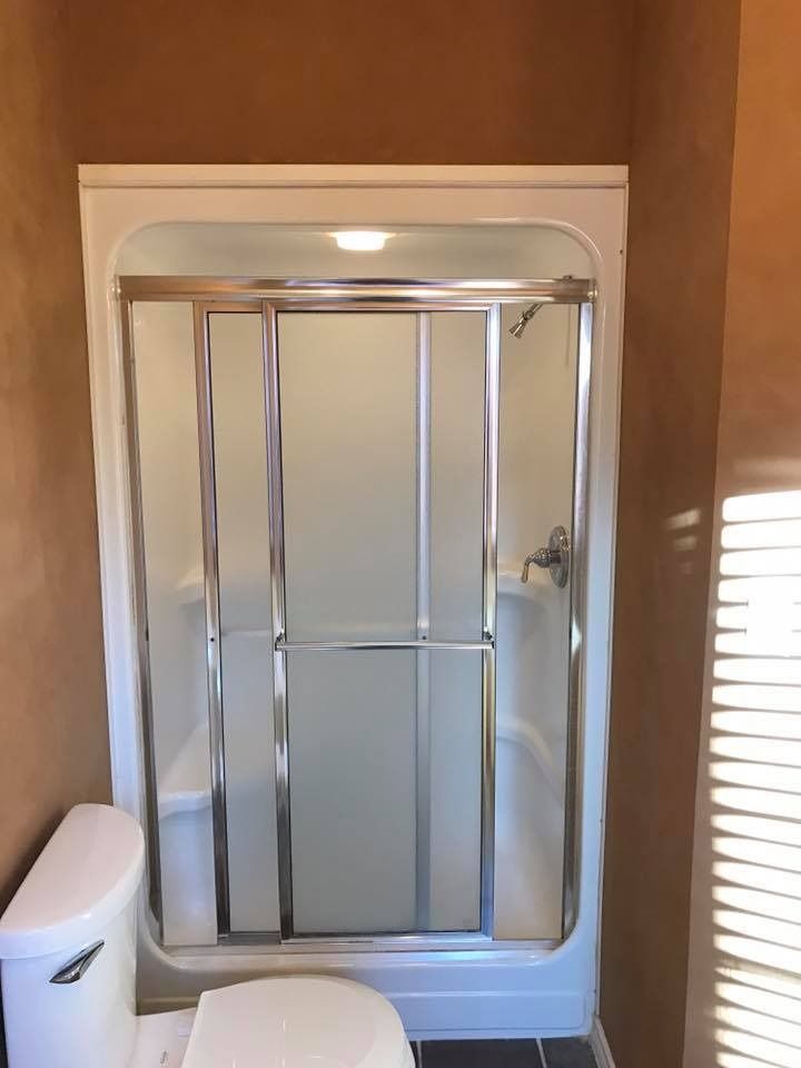 White framed shower with sliding glass doors, next to a toilet, in a bathroom with brown walls.