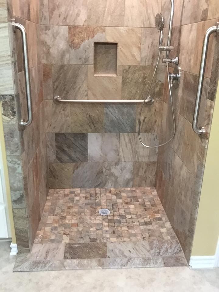 Walk-in shower with stone tile walls and floor, grab bars, and a built-in shelf.