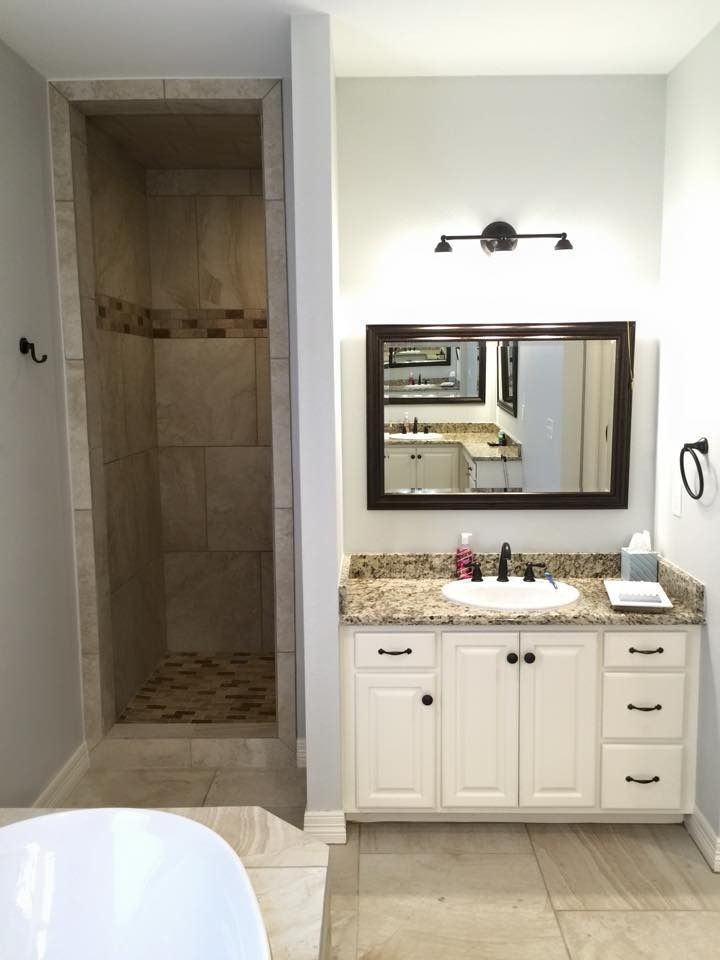 Bathroom with a tiled shower, white vanity, and large mirror.